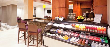A hotel lobby with a self-service beverage station, seating area, and a reception desk.