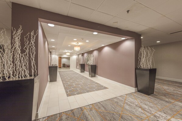 A modern hotel corridor with a geometric patterned carpet, recessed lighting, and decorative white sculptures.