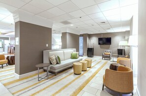 A modern hotel lobby with a sofa, armchairs, a flat-screen TV, and a dining area.