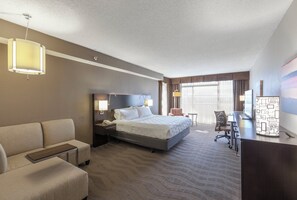 A hotel room with a bed, a desk, a chair, a sofa, and a lamp.