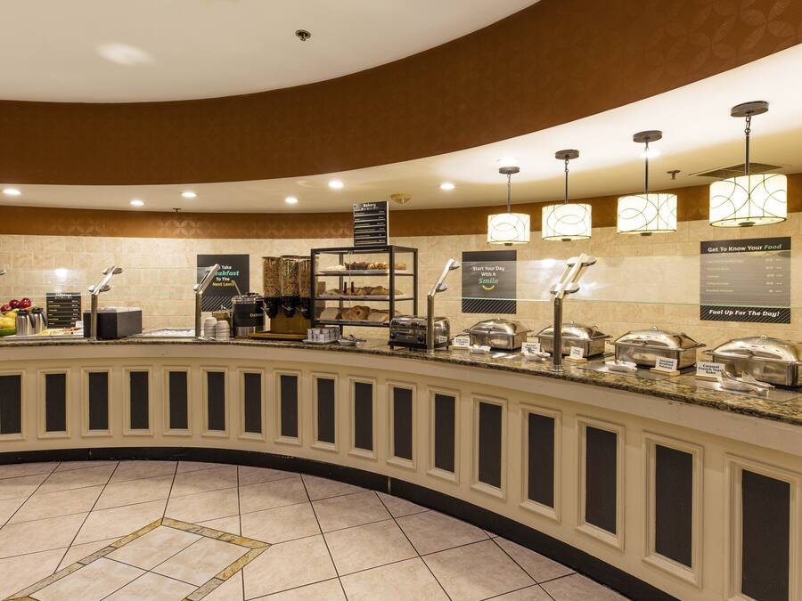 Un espace pour le petit-déjeuner à l’hôtel, doté d’un comptoir incurvé, d’un espace où l’on peut se servir soi-même du café et de différents présentoirs pour les aliments.