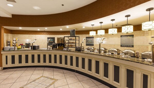 A hotel breakfast area with a curved counter, self-serve coffee station, and various food display cases. - Holiday Inn Austin Midtown by IHG (Austin)
