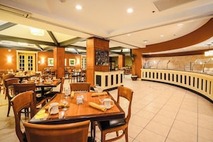 A hotel dining area with multiple tables and chairs, a buffet counter, and a peacock-themed wall decoration.