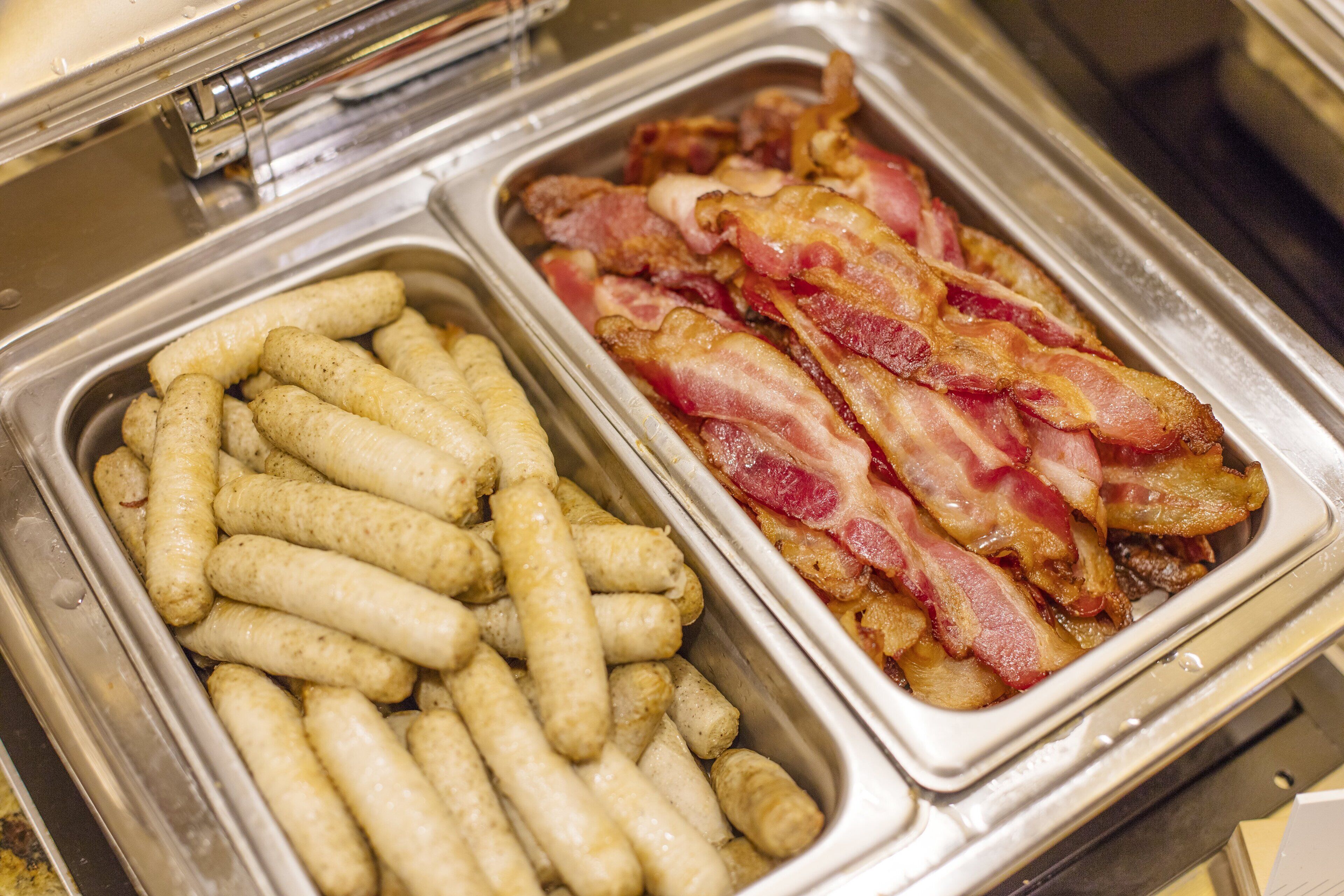 Un bufé con dos fuentes de comida: una con salchichas y otra con tocino.