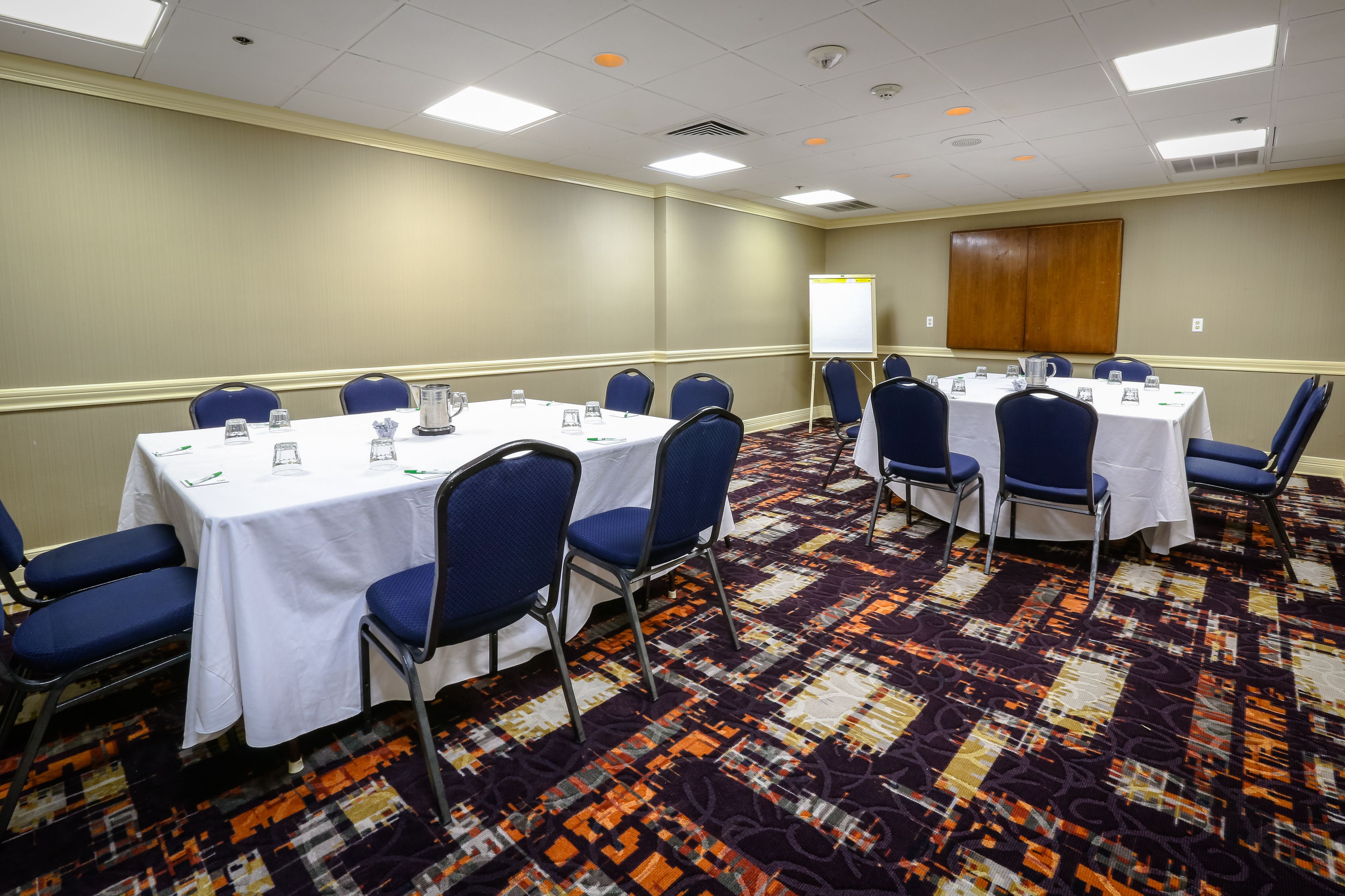 A conference room with tables and chairs, a whiteboard, and a carpeted floor.