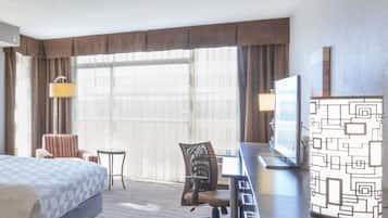 A hotel room with a bed, desk, chair, lamp, and a large window.