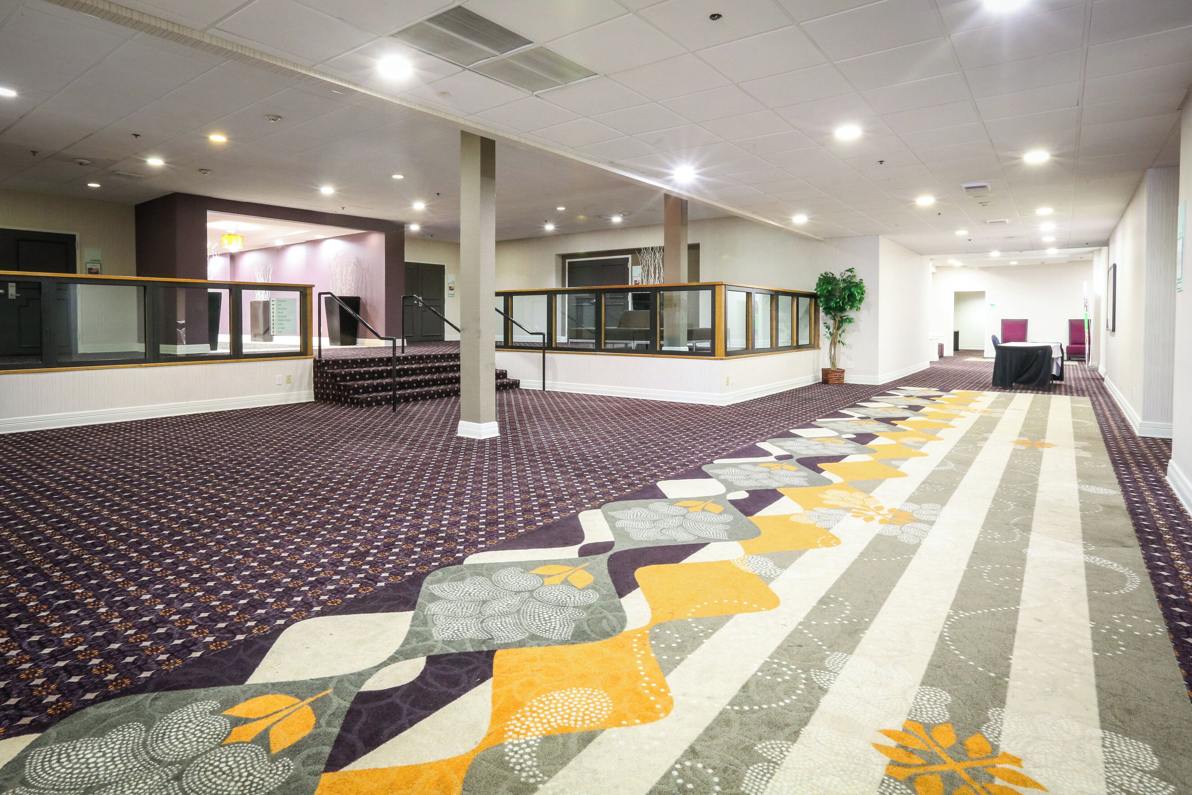 A hotel lobby with a patterned carpet, a staircase, and a reception desk.