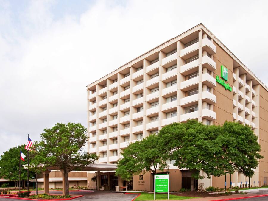 A multi-story hotel with a beige facade, a green logo, and a sign indicating amenities.