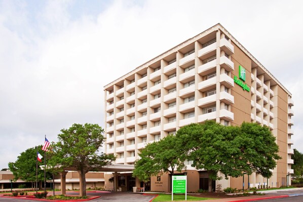 A multi-story hotel with a beige facade, a green logo, and a sign indicating amenities.