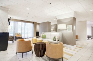 A modern hotel lobby with a sofa, chairs, a coffee table, and a TV.