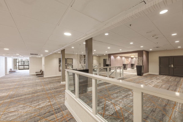A spacious hotel lobby with a high ceiling, recessed lighting, and a patterned carpet.