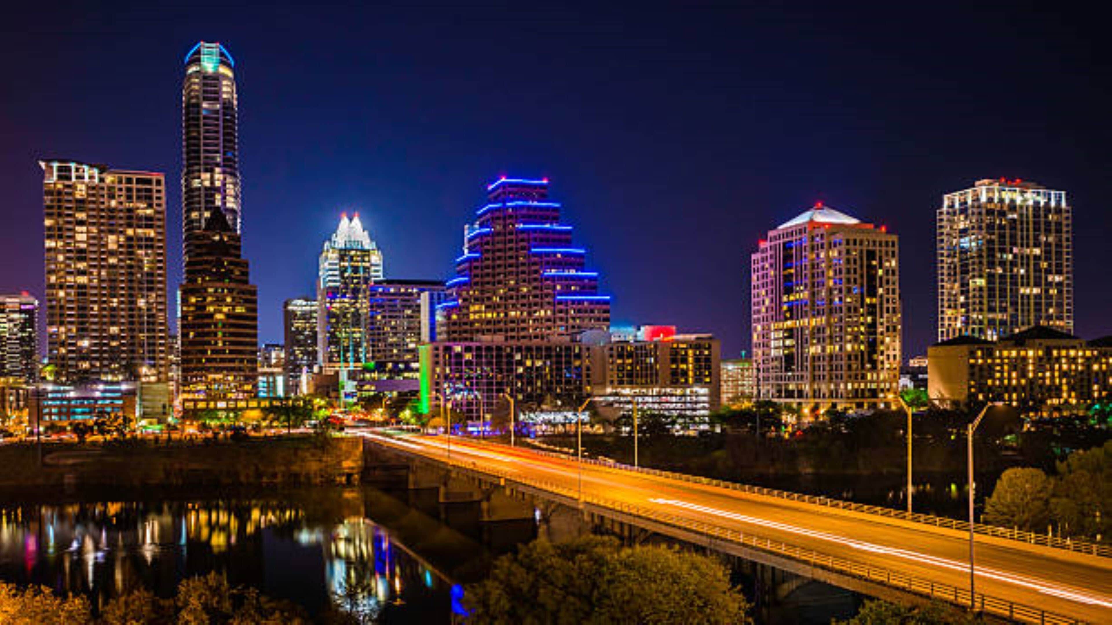 A city skyline with illuminated buildings and a bridge.