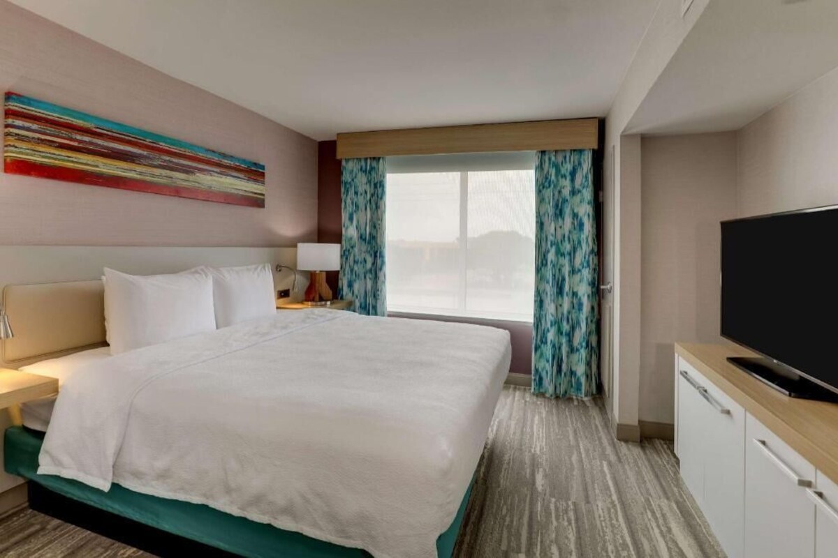 Una habitación de hotel con cama, televisión, escritorio y ventana con cortinas.