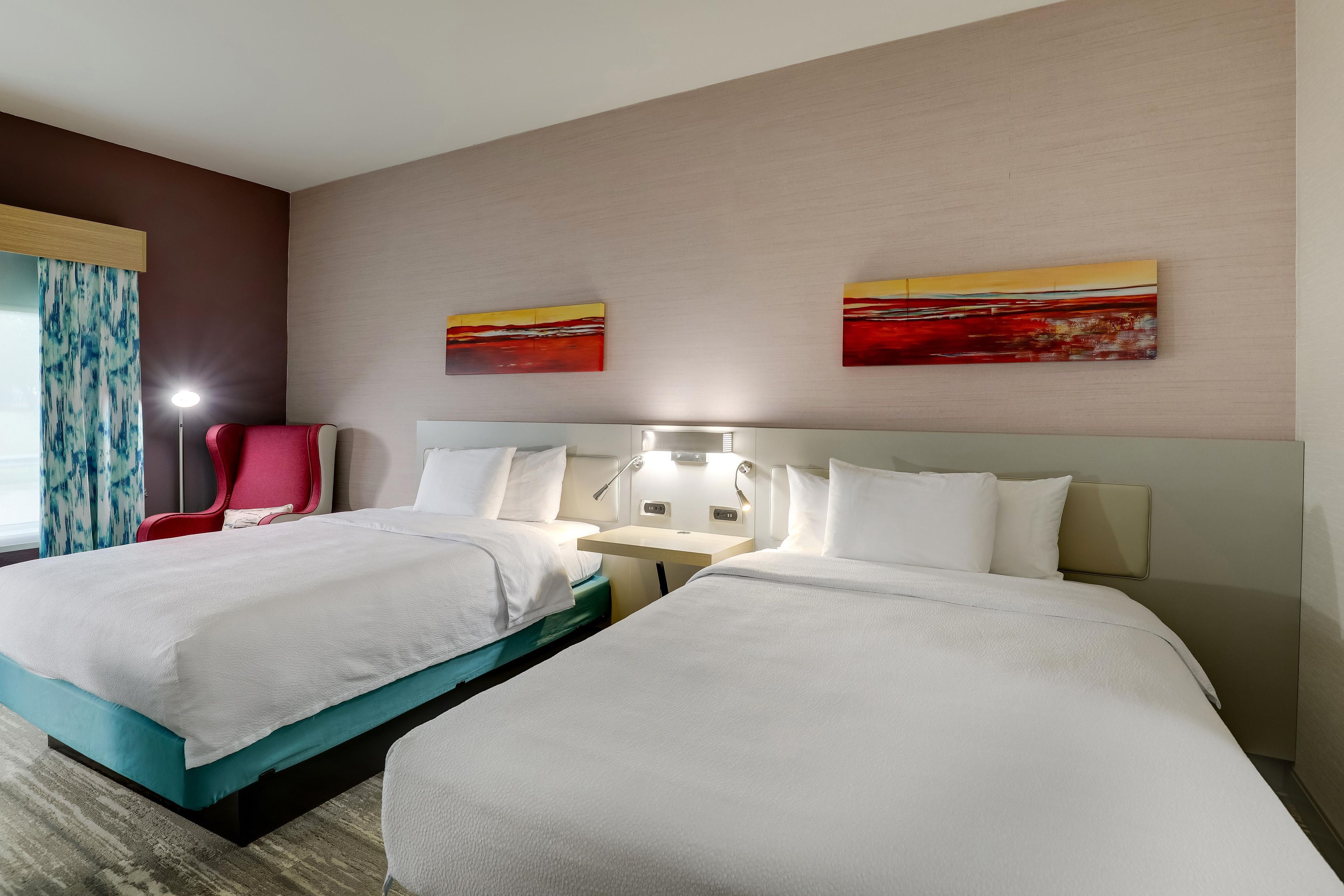 Ein Hotelzimmer mit zwei Betten, einem roten Sessel, einem Schreibtisch und zwei Bildern an der Wand.