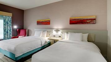 Ein Hotelzimmer mit zwei Betten, einem roten Sessel, einem Schreibtisch und zwei Bildern an der Wand.