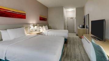 Habitación de hotel con dos camas, un escritorio y un televisor de pantalla plana, y una puerta que da a un baño.