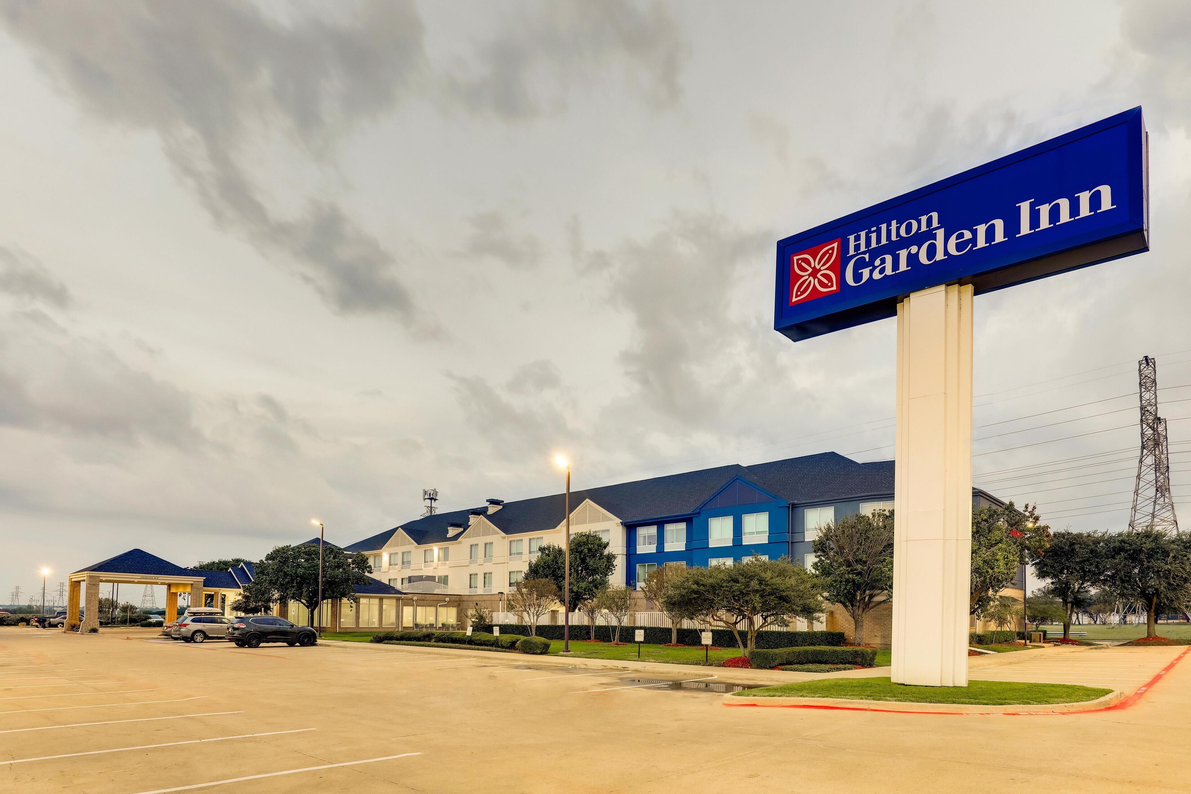 A Hilton Garden Inn with a large sign, a parking lot, and a row of buildings with blue roofs.
