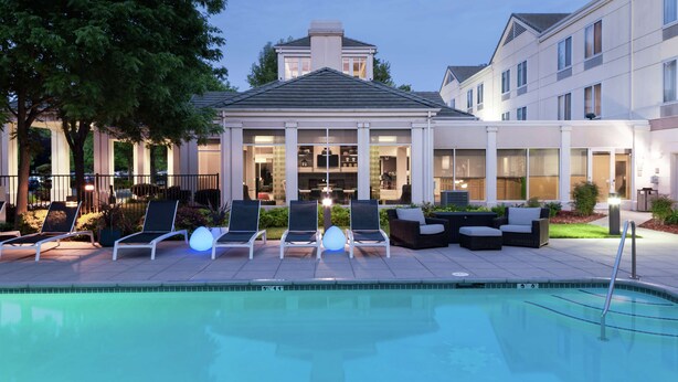 A poolside area with lounge chairs, a covered seating area, and a building with large windows.