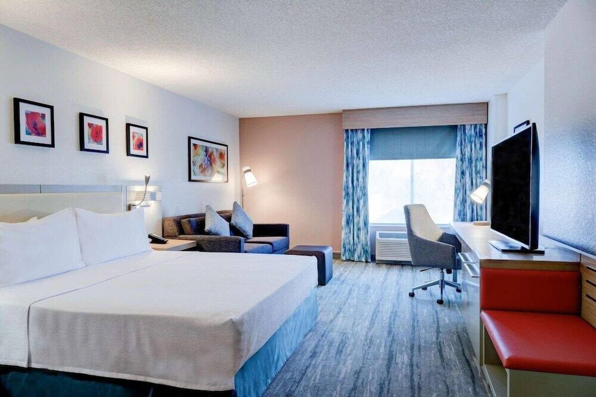 Una camera d'hotel con un letto, una scrivania, una sedia, una televisione e opere d'arte appese al muro.