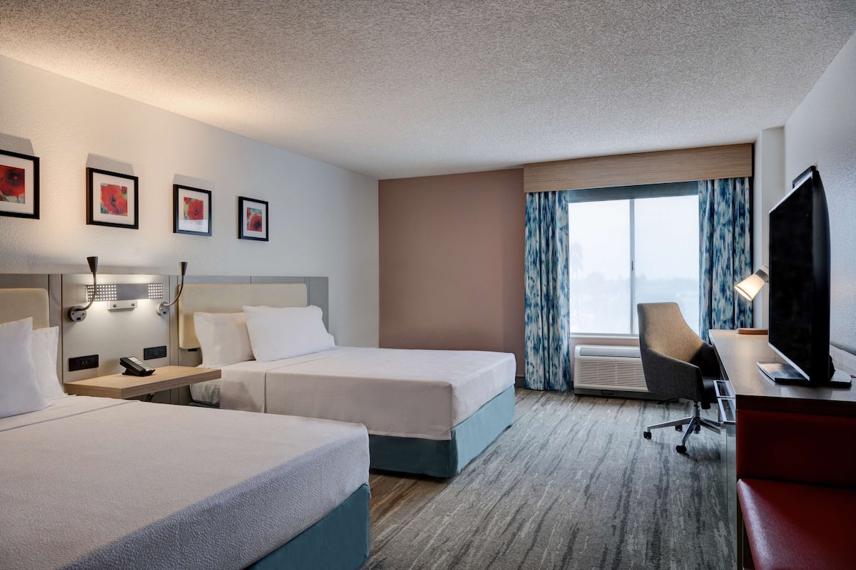 A hotel room with two beds, a desk with a chair, a television, and a window with curtains.