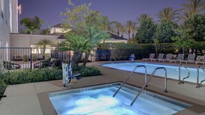 A swimming pool with lounge chairs and a hot tub, surrounded by palm trees and a fence. - Hilton Garden Inn Anaheim Garden Grove (Garden Grove)