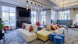 A spacious living area with a large sofa set, a flat-screen TV mounted on the wall, and a fireplace. - Hilton Garden Inn Anaheim Garden Grove (Garden Grove)