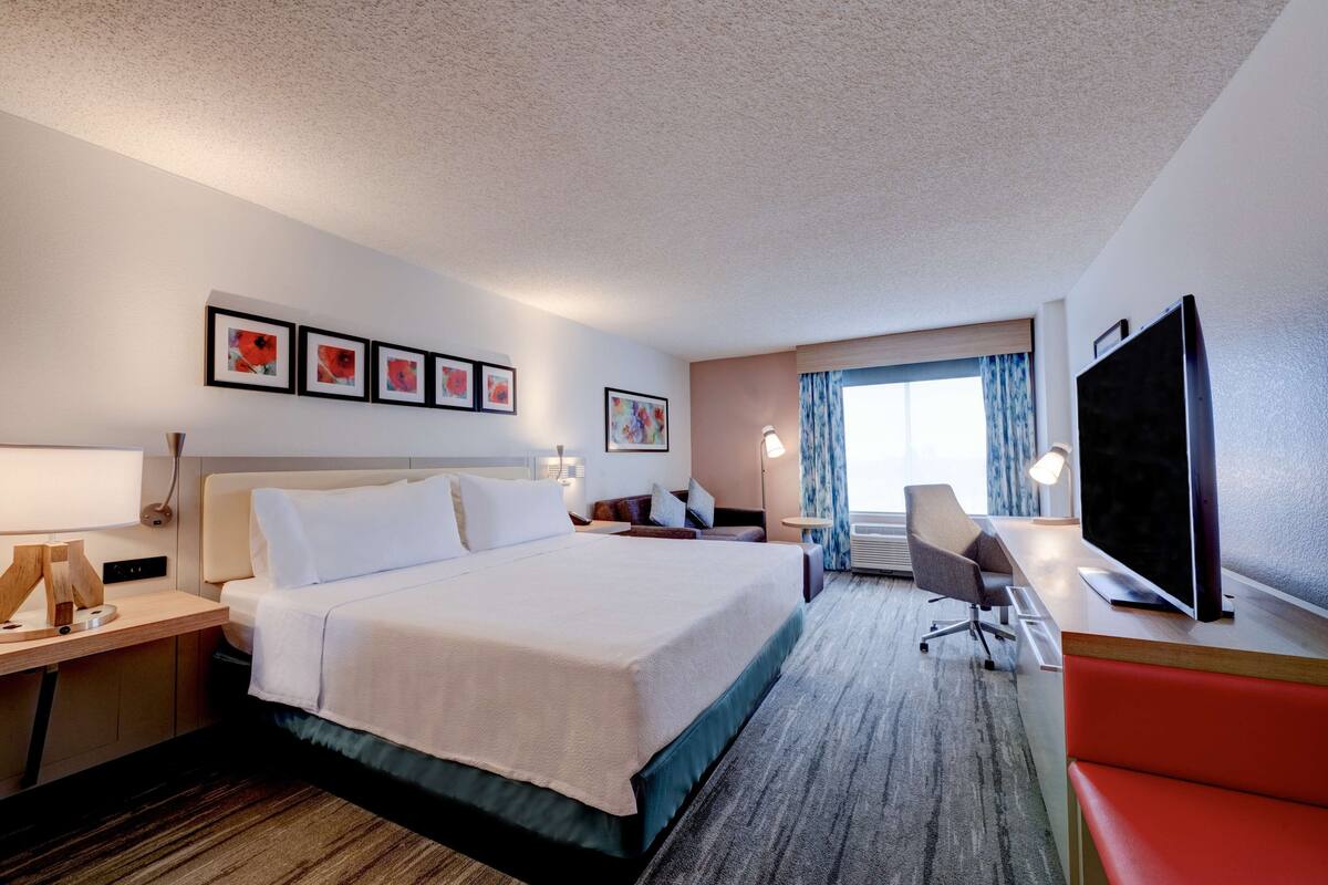 A hotel room with a large bed, a desk with a chair, a television, and artwork on the walls.
