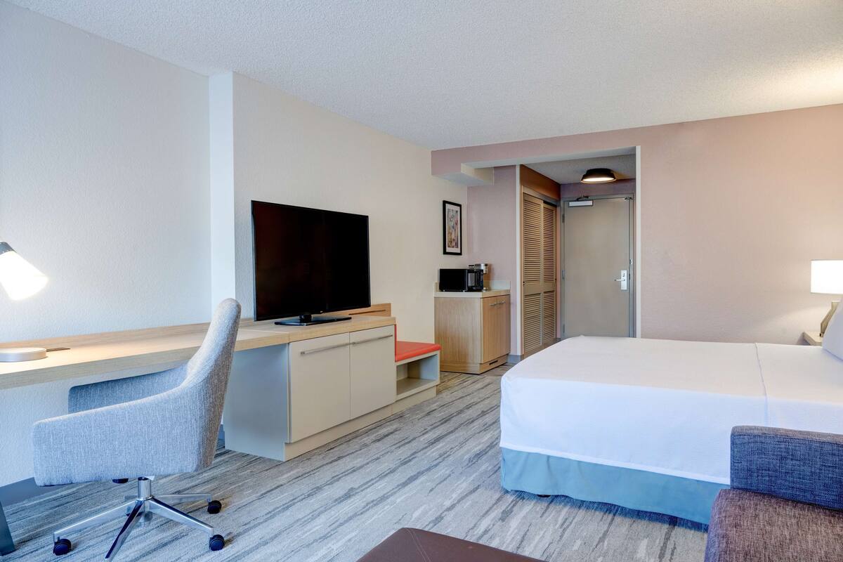 A hotel room with a bed, a desk with a chair, a television, and a wardrobe.