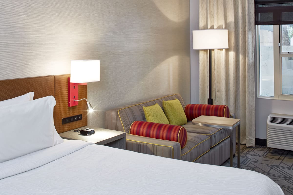 Ein Hotelzimmer mit einem Bett, einem Schlafsofa, zwei Nachttischlampen, einem Nachttisch und einer Klimaanlage.