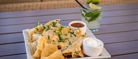 A plate of nachos with a creamy sauce and a side of sour cream, accompanied by a glass of iced tea with a mint garnish.