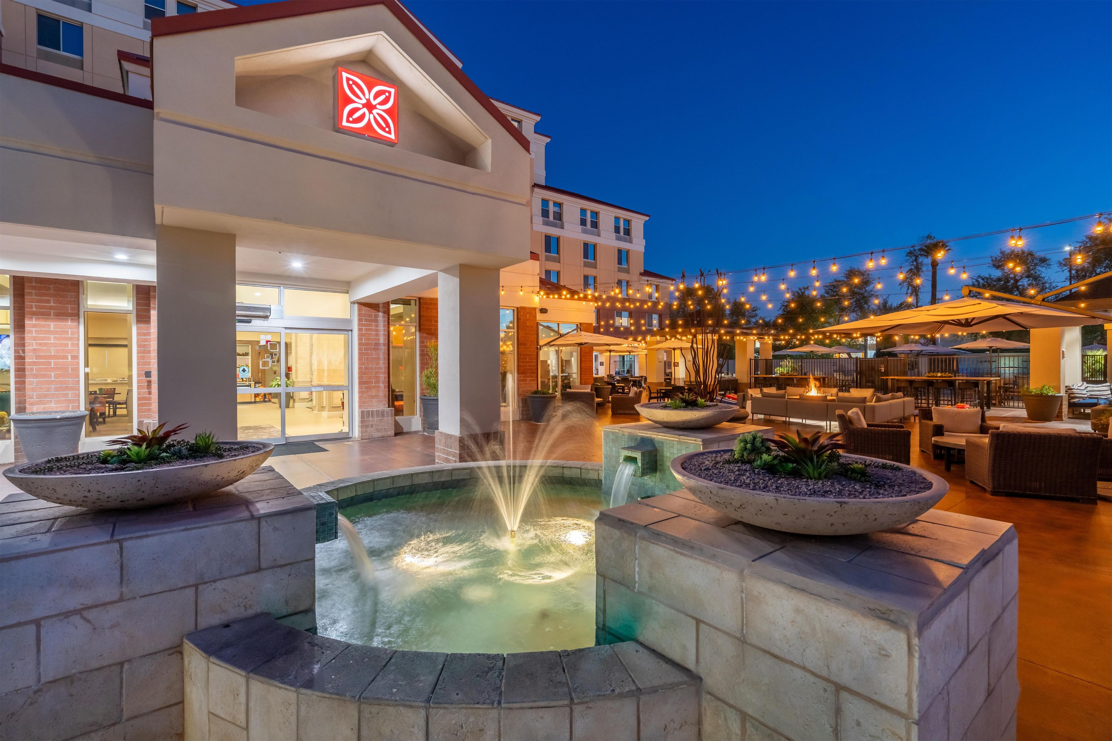 Un patio de hotel con una fuente, asientos al aire libre y luces colgantes.