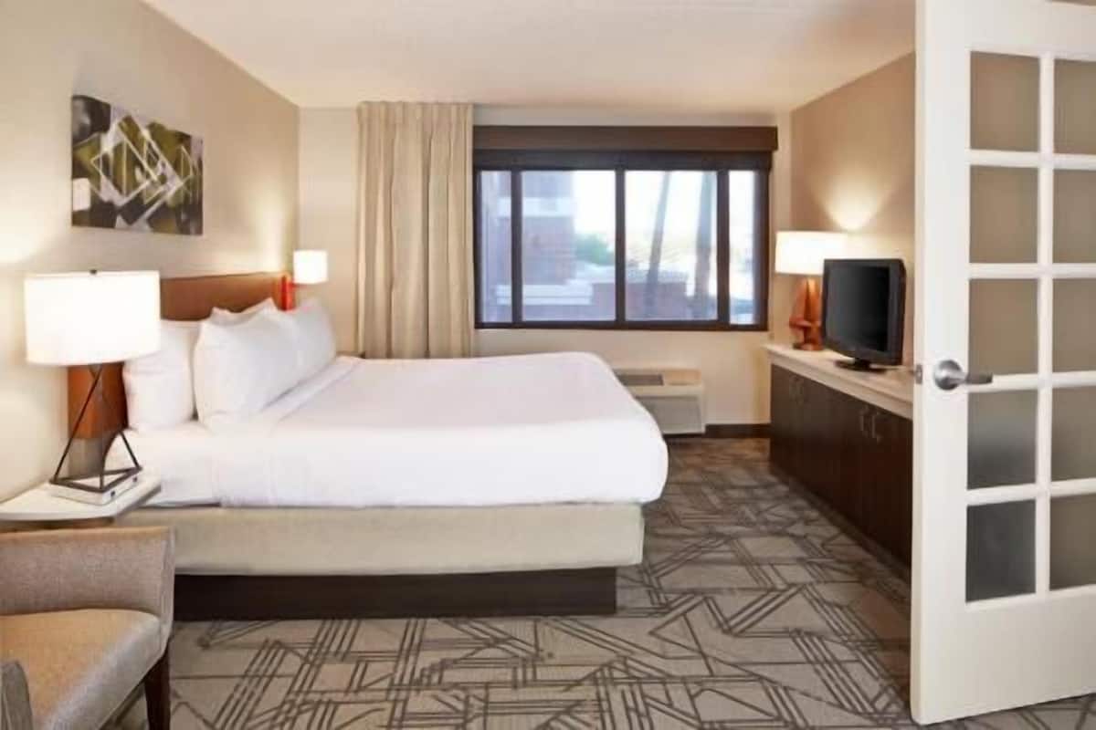 Ein Hotelzimmer mit einem Bett, einem Schreibtisch, einem Fernseher und einem Fenster mit Vorhängen.