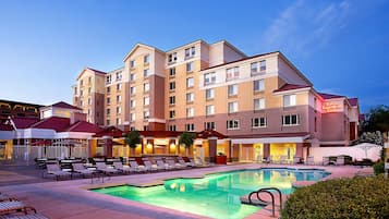 A hotel with a swimming pool, outdoor seating, and a well-lit facade.