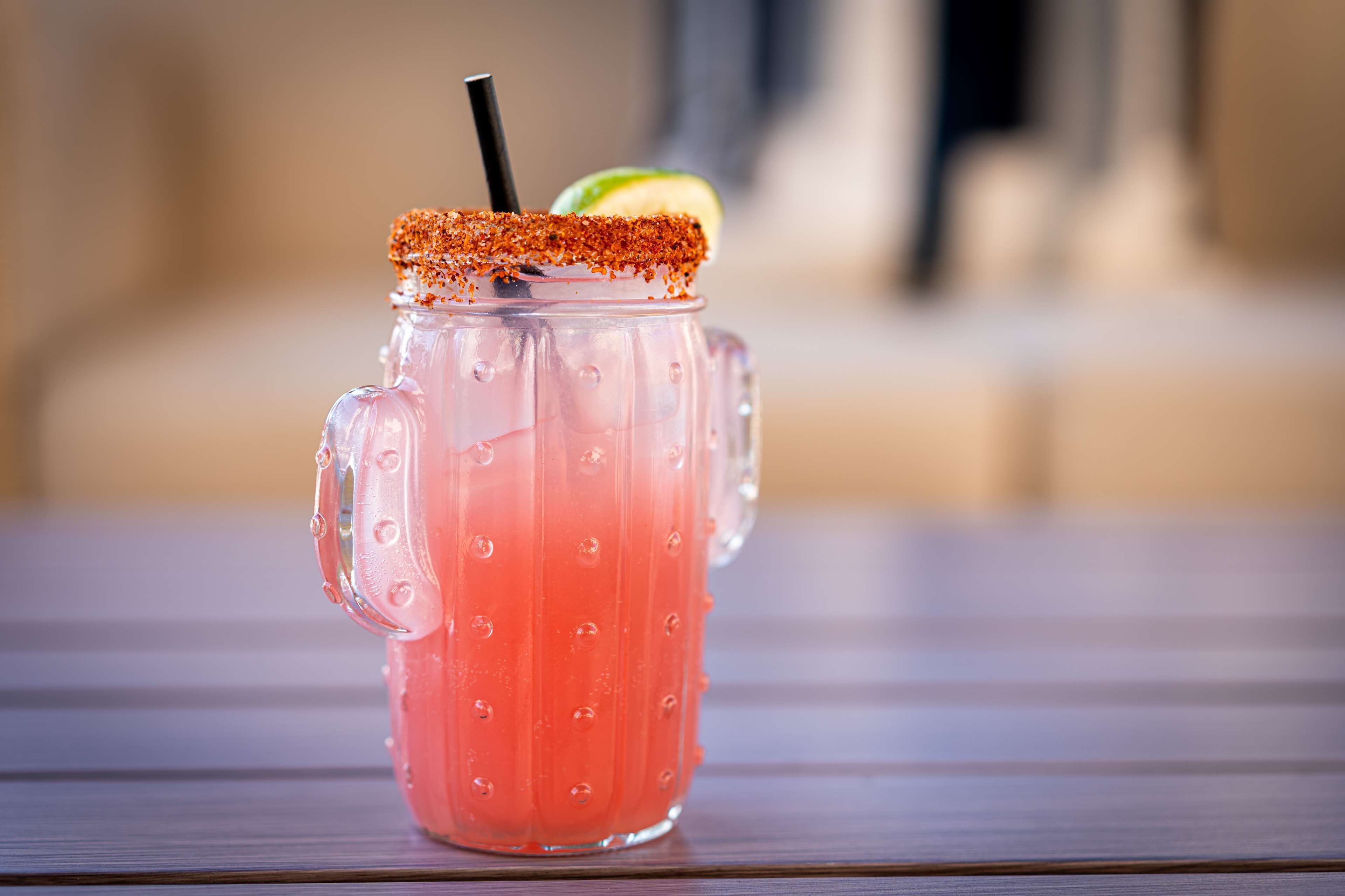 A clear glass beverage with a salted rim and a straw, placed on a wooden surface.