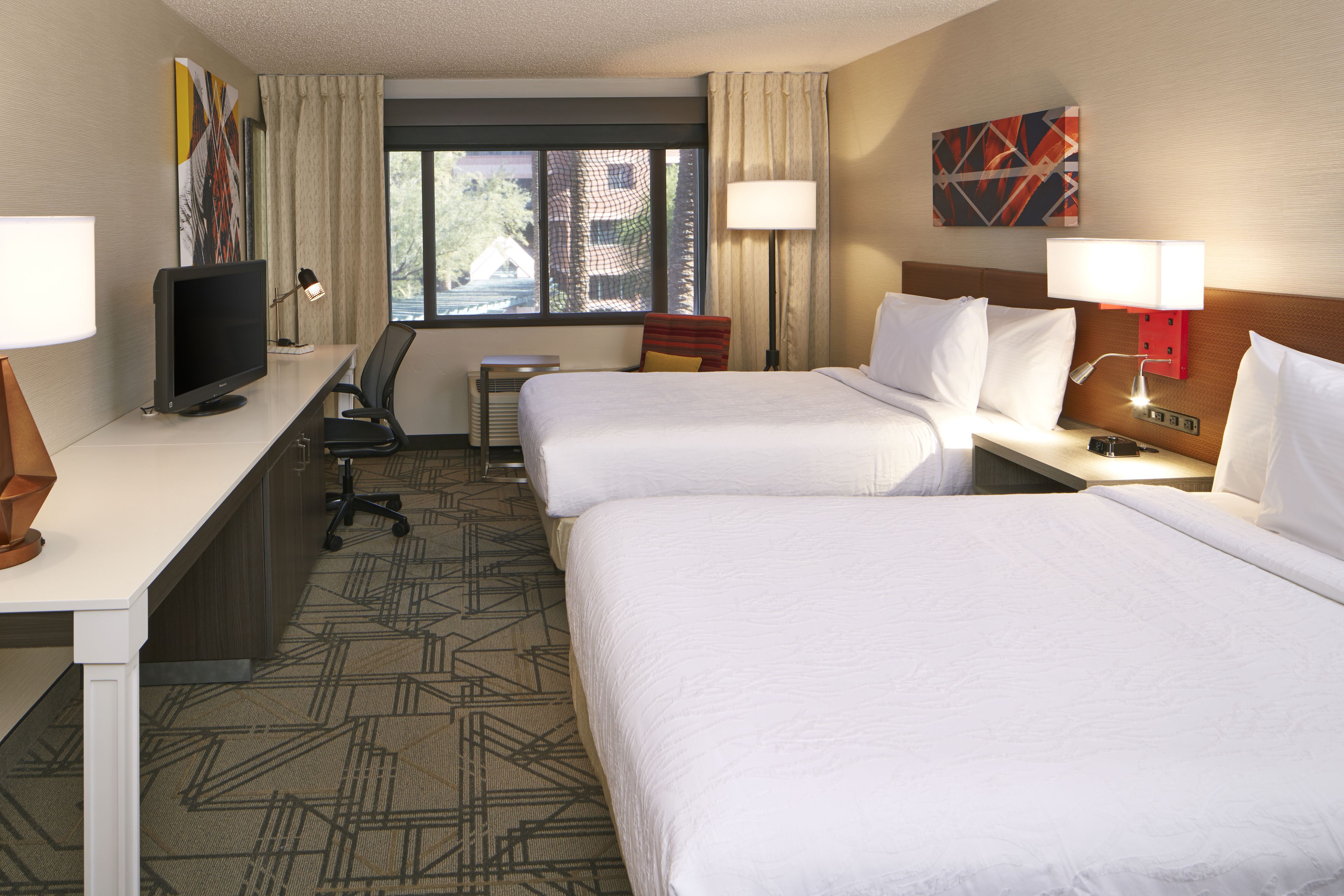 A hotel room with two beds, a desk with a computer, a chair, and a TV.