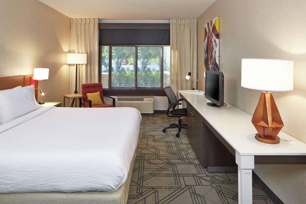 Ein Hotelzimmer mit einem großen Bett, einem Schreibtisch mit Computer, einem Stuhl und einem Fernseher.