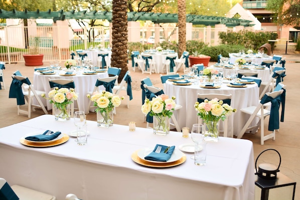 An outdoor dining area with round tables, white tablecloths, and blue chair covers. - Hilton Garden Inn Scottsdale Old Town (Scottsdale)