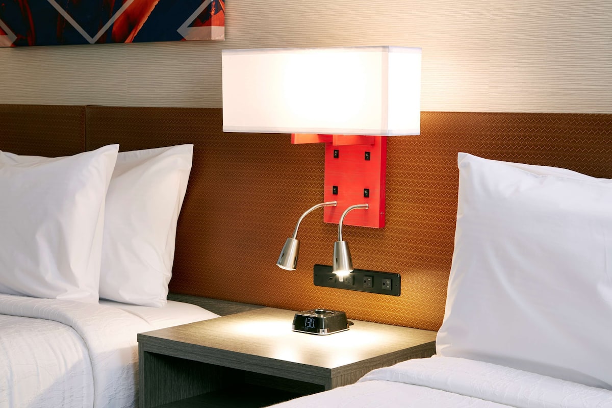 Ein Hotelzimmer mit einem Bett, einem Nachttisch, einer digitalen Uhr und einer Wandlampe.