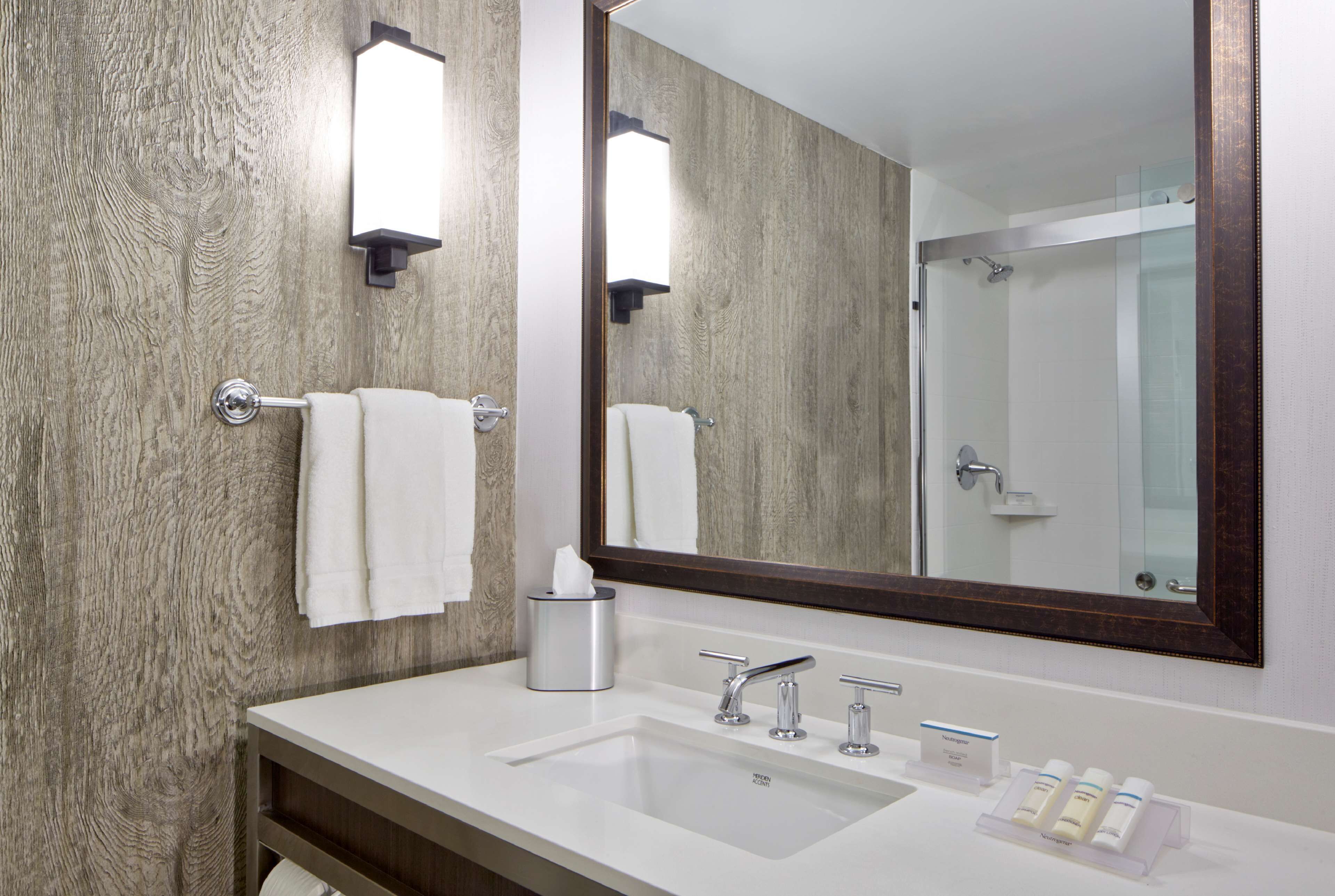 Un baño con pared de madera, un espejo grande, un lavamanos blanco y una cabina de ducha de vidrio.