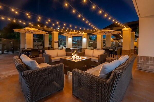 An outdoor seating area with wicker furniture, a central fire feature, and string lights.