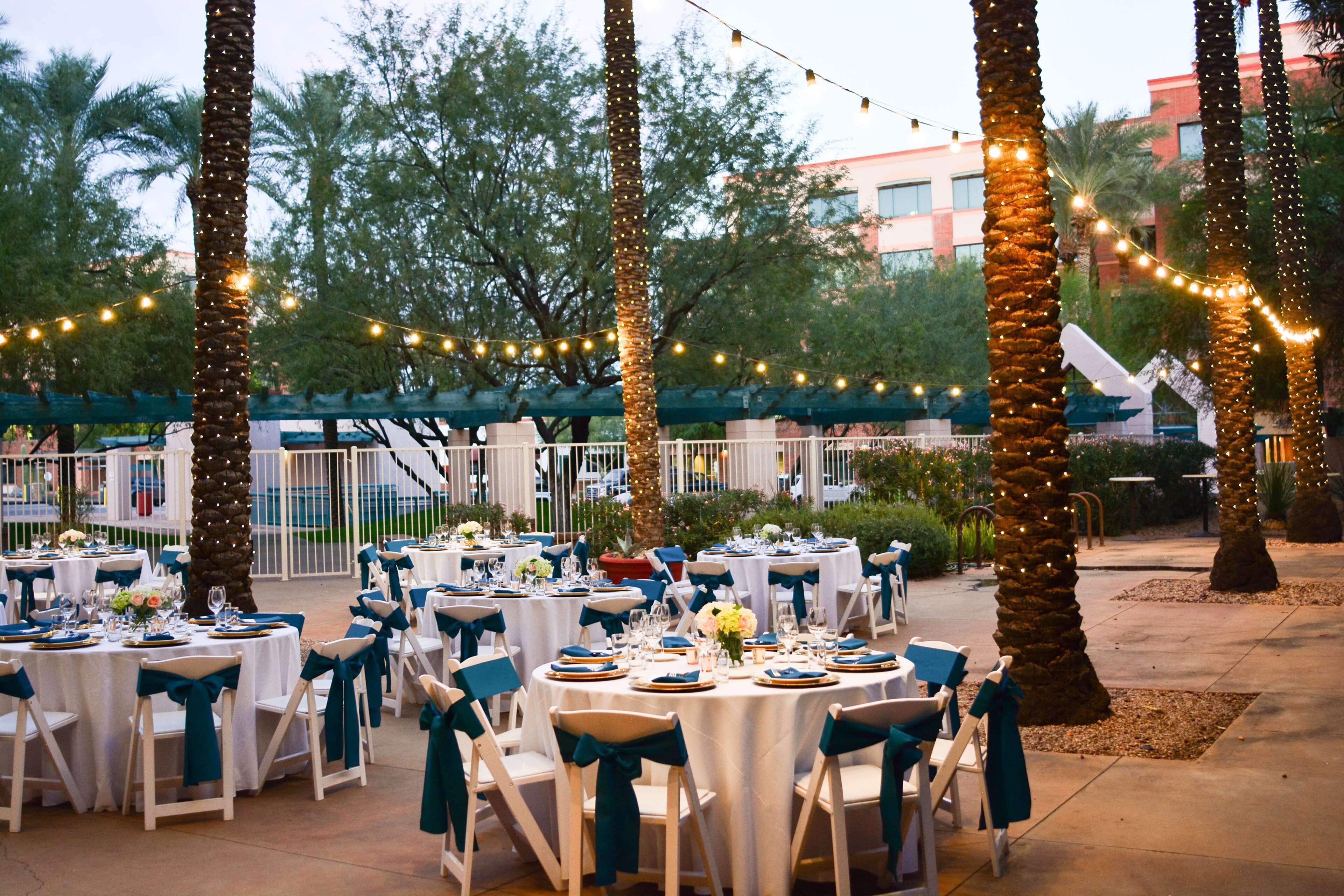An outdoor dining area with round tables, white tablecloths, and chairs with teal sashes.