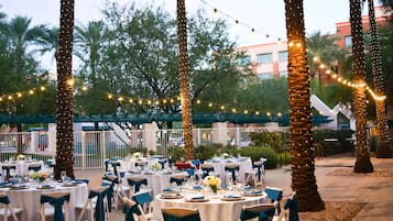 An outdoor dining area with round tables, white tablecloths, and chairs with teal sashes.