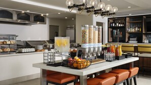 A modern kitchen with a central island, bar stools, and a variety of food items and condiments. - Hilton Garden Inn San Jose/Milpitas (Milpitas)