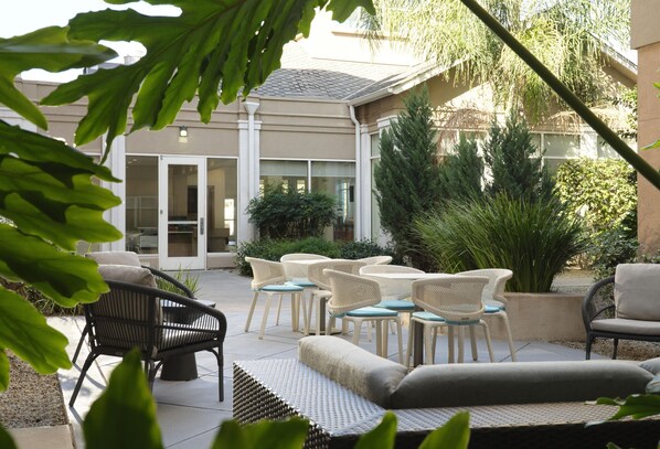 An outdoor patio with wicker furniture, a seating area, and a view of a building with a glass door.