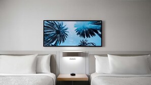 A hotel room with two beds, a nightstand, a wall-mounted light, and a framed picture of palm trees. - Hilton Garden Inn San Jose/Milpitas (Milpitas)
