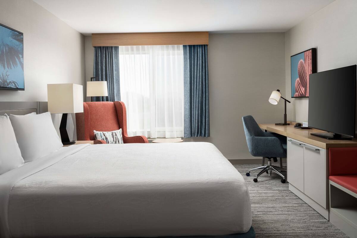 A hotel room with a large bed, a desk with a computer, a chair, and a TV.