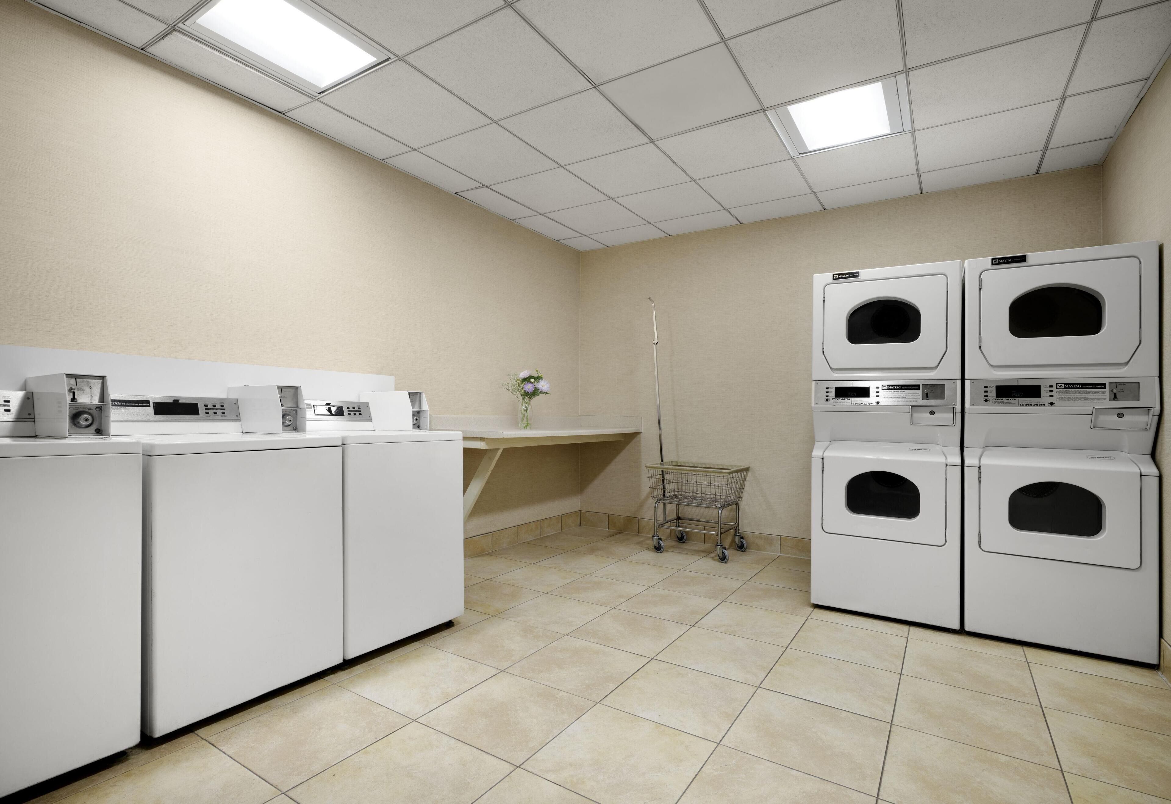 A laundry room with stacked washers and dryers, a small cart, and a tiled floor.