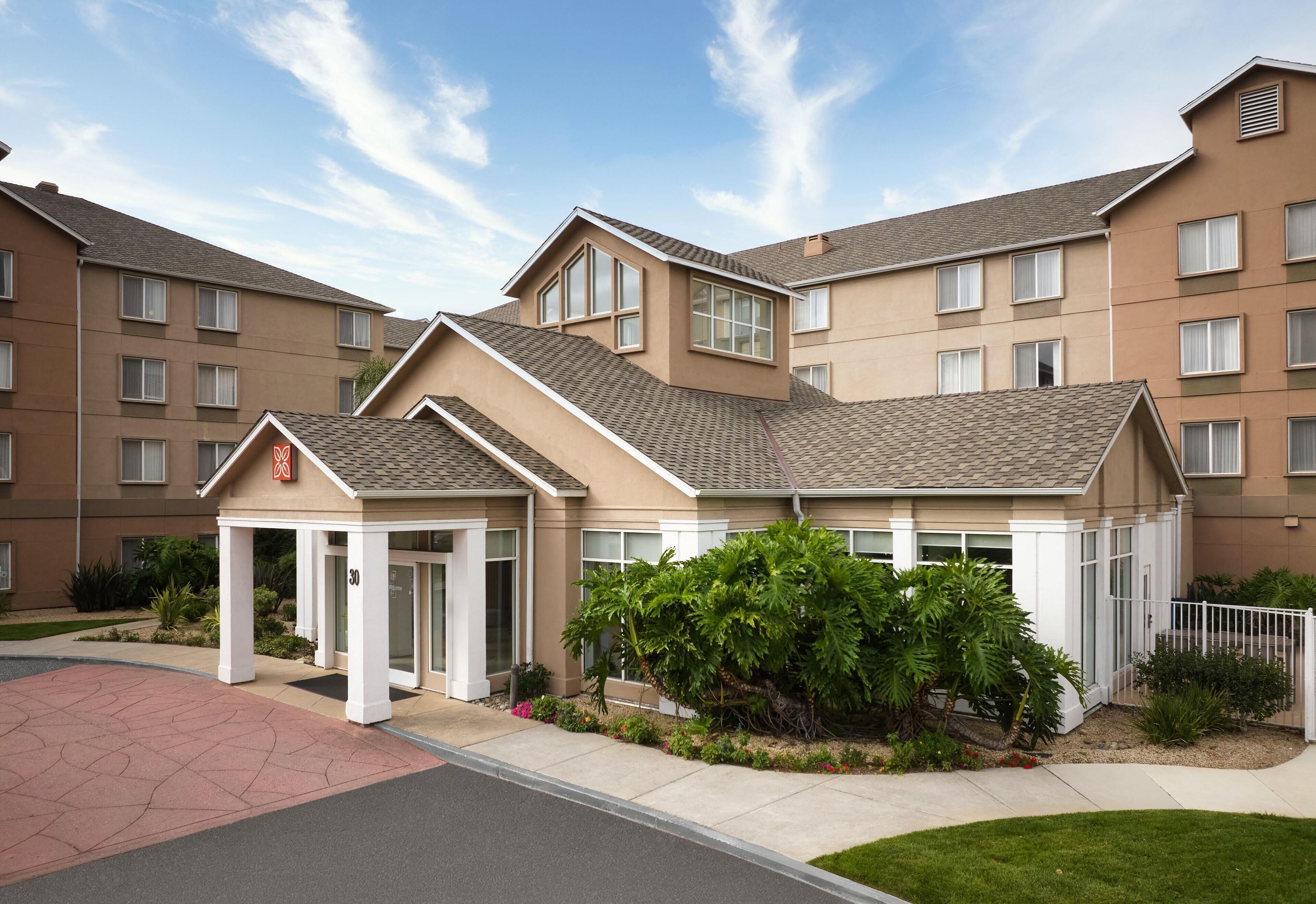 A multi-story hotel with a beige exterior, a covered entrance, and a well-maintained garden area.