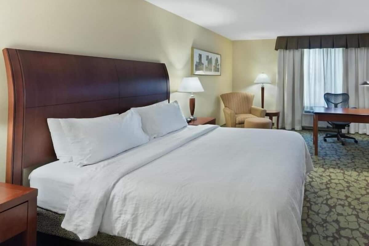 A hotel room with a large bed, a desk, a chair, and a lamp.
