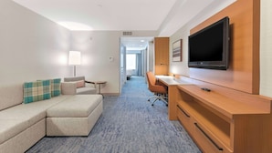 Ein Hotelzimmer mit einer Eckcouch, einem Schreibtisch mit Flachbildfernseher und einer Lampe.